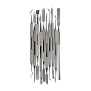 May include: A set of 12 stainless steel cuticle pushers with various shapes and sizes. The tools are arranged vertically on a white background.