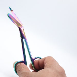 May include: Rainbow-colored surgical scissors with a curved blade, held in a hand.
