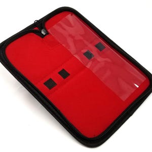 May include: A red zippered case with a clear plastic window and black elastic loops for holding small items. The case is made of a soft, padded material.