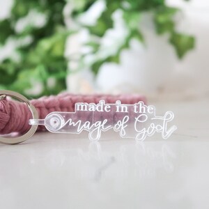 May include: A pink braided keychain with a clear acrylic charm that says "made in the image of God".