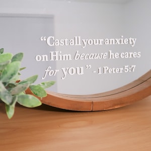 May include: A round mirror with a wooden frame and a white vinyl quote that reads "Cast all your anxiety on Him because he cares for you" - 1 Peter 5:7.