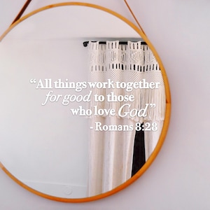 Könnte beinhalten: Ein runder Spiegel mit einem Holzrahmen spiegelt eine weiße Wand mit einem weißen Häkelvorhang wider. Der Spiegel spiegelt ein Zitat wider: "Alle Dinge arbeiten zum Guten zusammen für diejenigen, die Gott lieben" - Römer 8:28.