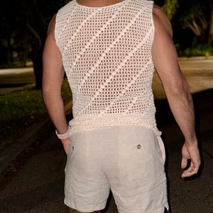 May include: A white crocheted sleeveless top with a diamond pattern and a pair of white linen shorts.