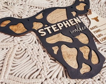 Könnte beinhalten: Ein hölzernes Schild in Kuhform mit einem schwarzen und braunen Holzmaserungsmuster. Das Schild trägt den Namen "STEPHEN walker". An dem Schild ist ein kleines Schild befestigt, auf dem die Wörter "DATE", "TIME", "LBS" und "LENG" stehen.