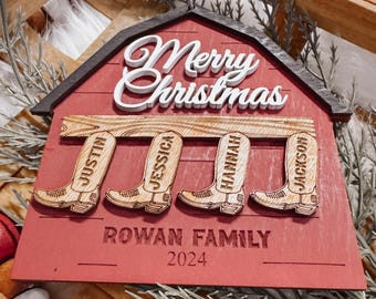 May include: Red wooden barn-shaped Christmas ornament with the words "Merry Christmas" on the front. The ornament has four wooden boots hanging from it with the names "Justin", "Jessica", "Hannah", and "Jackson" on them. The bottom of the ornament says "Rowan Family 2024".