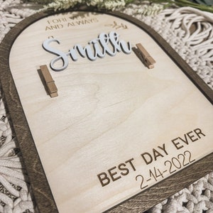 Może przedstawiać: Drewniany znak z brązową ramą i jasnym drewnianym tłem. Znak zawiera tekst "Forever and Always Smith" białymi literami i "Best Day Ever 2-14-2022" brązowymi literami. Na znaku znajdują się dwa drewniane spinacze.