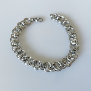 May include: A silver chain bracelet with a unique interlocking design. The bracelet is made of metal and has a polished finish.