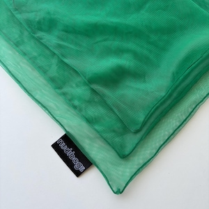 May include: Close-up of three layers of bright green mesh bags. The bags are folded and stacked, with the top layer slightly smaller than the others. A black tag with the word "nudibags" in white is visible.