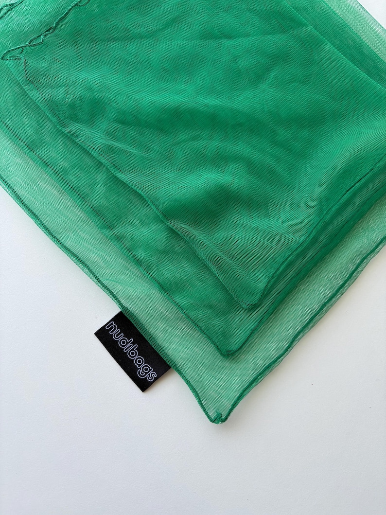 May include: Close-up of three layers of bright green mesh bags. The bags are folded and stacked, with the top layer slightly smaller than the others. A black tag with the word "nudibags" in white is visible.
