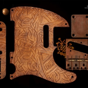 Könnte beinhalten: Eine Sammlung von Gitarrenteilen, darunter ein Schlagbrett, eine Steuerplatte und eine Brücke, alle in warmbrauner Farbe. Das Schlagbrett weist ein aufwendiges Schnitzmuster auf. Der Text "Pick Art Hand Made Guitars Pickguards" ist enthalten.
