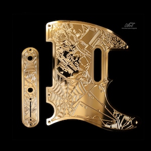 Op de afbeelding: Een goudkleurige metalen slagplaat en controleplaat voor een gitaar met gedetailleerde gravures van een schedel, spinnenweb en speelkaarten. Het oppervlak is gepolijst en reflecterend, voorzien van de tekst Art Pick Hand Made Guitar Pickguards.
