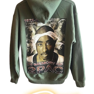 May include: A green hooded sweatshirt with a large print of rapper 2Pac on the back. The print includes the text "1971-1996" and "In Memory of 2Pac".