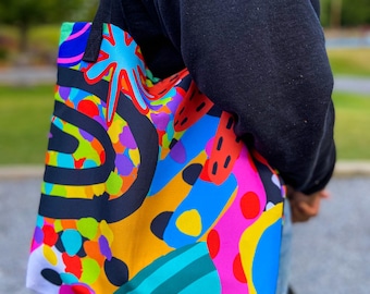 Peut inclure: Un sac fourre-tout coloré avec un motif abstrait noir, jaune, bleu, rose, vert et rouge. Le sac a deux anses noires.