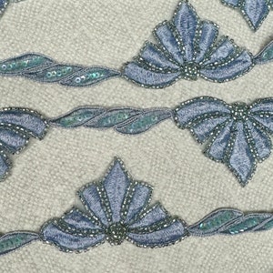 Puede incluir: Primer plano de una cinta de cuentas azules con un diseño festoneado. La cinta está hecha de pequeñas cuentas iridiscentes que están cosidas juntas en un patrón repetitivo. La cinta es perfecta para agregar un toque de elegancia a cualquier proyecto.