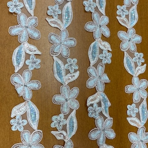 Peut inclure: Garniture florale bleu clair avec des paillettes et des perles. La garniture est faite d'un tissu transparent et a un aspect délicat et féminin.