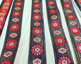 Puede incluir: Borde negro y rojo con un patrón floral. El borde está hecho de tejido tejido y tiene un hilo metálico dorado.