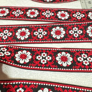 May include: Four different widths of black, red and white patterned ribbon with a floral design. The ribbon is woven with small white flowers and larger white flowers with red centres.