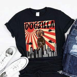 May include: Black t-shirt with a graphic of a brown dog standing in front of a red and white rising sun with the text "DOGZILLA" above the dog.