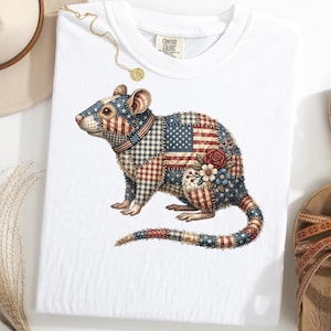 Könnte beinhalten: Weißes T-Shirt mit einer detaillierten Illustration einer Ratte. Das Rattendesign integriert die amerikanische Flagge, Sterne und Streifen in einem Patchwork-Stil. Es hat einen rot-weiß-blauen Kragen und florale Akzente. Das T-Shirt wird mit Sandalen und einem Hut präsentiert.