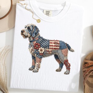 以下が含まれることがあります： パッチワークデザインの犬の精巧なイラストが描かれた白いTシャツ。犬の毛皮には、アメリカ国旗、花、チェック柄の要素が組み込まれています。Tシャツはサンダルと帽子でスタイリングされています。