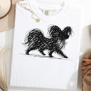 May include: White t-shirt featuring a black scribble-style illustration of a dog. The dog is depicted in a walking pose. The shirt has a crew neck and short sleeves. The brand tag is visible on the upper right side of the shirt.