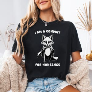 May include: Black t-shirt with a graphic of a fox wearing a cape and holding a sword. The text "I am a conduit for nonsense" is printed below the fox.