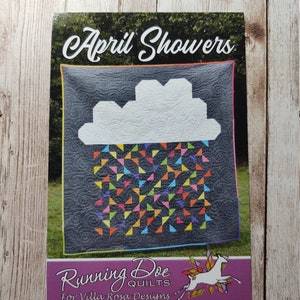 May include: A quilt pattern titled "April Showers" featuring a gray background with a white cloud and colorful triangle rain. The pattern is from Running Doe Quilts for Villa Rosa Designs.