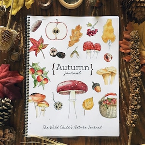 Könnte beinhalten: Ein Spiralbuch mit dem Titel "Autumn Journal" mit Aquarellillustrationen von Herbstmotiven wie Pilzen, Blättern und Äpfeln. Das Buch ist geöffnet und zeigt farbenfrohe Zeichnungen auf einer Holzoberfläche.