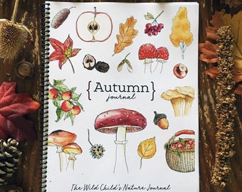 May include: A spiral-bound journal titled "Autumn Journal" with watercolor illustrations of fall elements like mushrooms, leaves, and apples. The journal is open, displaying colorful drawings on a wooden surface.