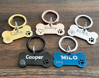 May include: Five dog bone-shaped pet ID tags with different engravings. The tags are gold, rose gold, silver, black, and blue. The engravings include the names "Luna", "Daisy", "Bear", "Cooper", and "Milo".