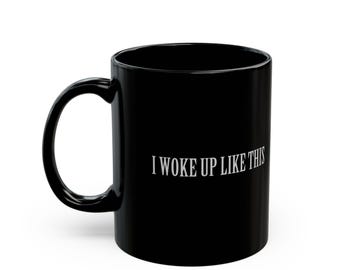 Può includere: Una tazza da caffè in ceramica nera con una scritta bianca che dice "I woke up like this".