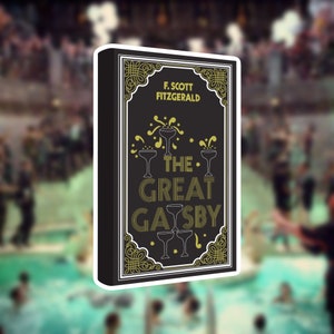 May include: A sticker featuring the book cover of "The Great Gatsby" by F. Scott Fitzgerald. The design has a black background with gold and white text and illustrations of champagne glasses. The sticker has a white border.