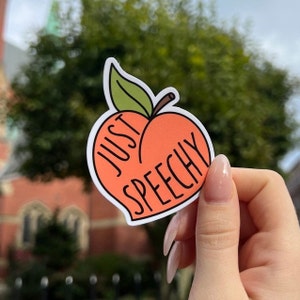 May include: A peach-shaped sticker with a green leaf and stem. The peach is orange and has the text "Just Peachy" written on it.
