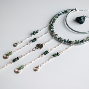 May include: A silver wire crescent moon with green agate stones and a larger green agate stone hanging from the center.  Four strands of silver chain hang from the crescent moon, each with a green agate stone and a silver spiral at the end.