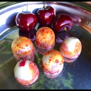 May include: A silver platter holds fresh cherries and decorated chocolate bonbons. The cherries are a deep red with glossy skin. The bonbons are round, with a white base and orange and red speckled designs.