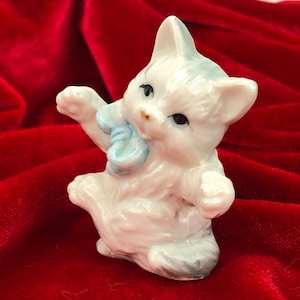 Miniaturowa figurka zabawnego kotka, biały porcelanowy kotek, mały kociak z niebieską wstążką