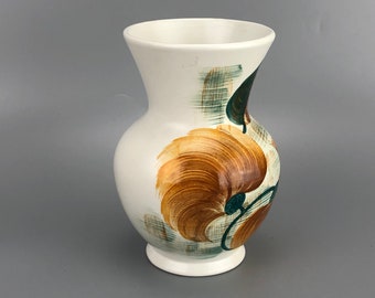 Könnte beinhalten: Weiße Keramikvase mit bauchigem Körper und ausgestelltem Rand. Die Vase hat ein großes Blumendesign in Braun-, Grün- und Türkistönen. Das Design ist auf weißem Hintergrund gemalt. Die Vase hat einen runden Sockel.