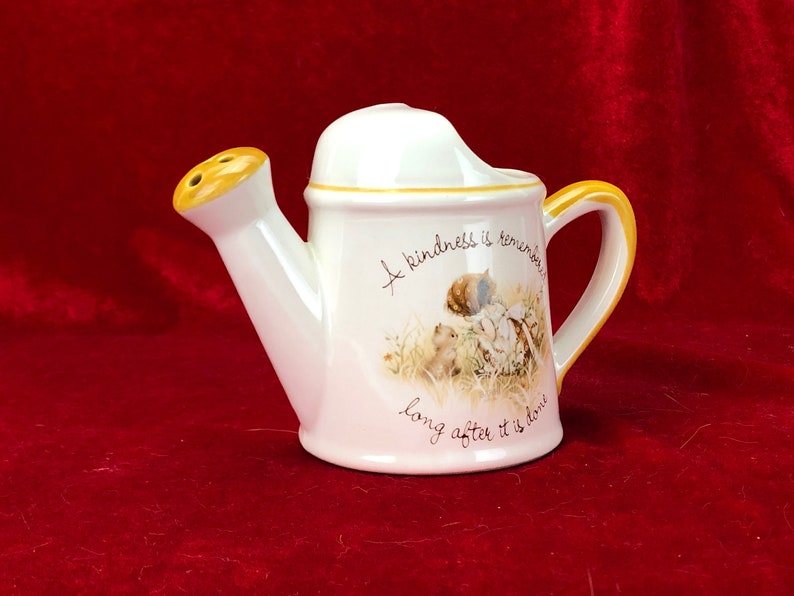 Pode incluir: Regador de cer&acirc;mica branca com um bico e uma al&ccedil;a amarelos. Tem um design floral e o texto "A kindness is remembered long after it is done".