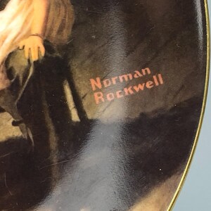 May include: A round ceramic plate with a gold rim features a painting of a young girl in a white dress sitting on a chair. The plate has the artist's signature, "Norman Rockwell", printed in red on the bottom right corner.
