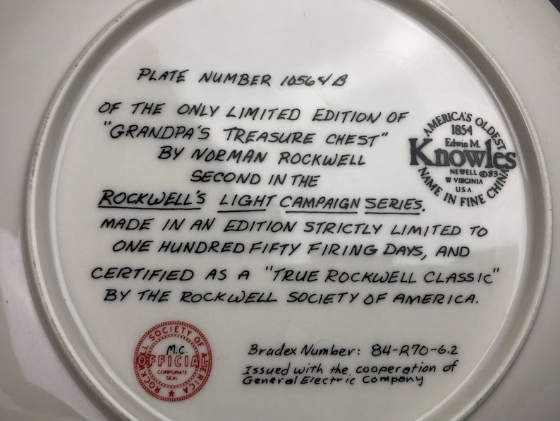 May include: A white ceramic plate with black text on the back. The text reads "Plate Number 10564 B of the only limited edition of "Grandpa's Treasure Chest" by Norman Rockwell Second in the Rockwell's Light Campaign Series. Made in an edition strictly limited to one hundred fifty firing days, and certified as a "True Rockwell Classic" by the Rockwell Society of America. Bradex Number: 84-R70-6.2 Issued with the cooperation of General Electric Company."