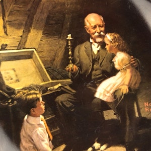 May include: A vintage-style porcelain plate featuring a painting by Norman Rockwell. The painting depicts an older man with a white beard, holding a candlestick, and two children looking at a treasure chest. The plate has a black background with a gold rim.