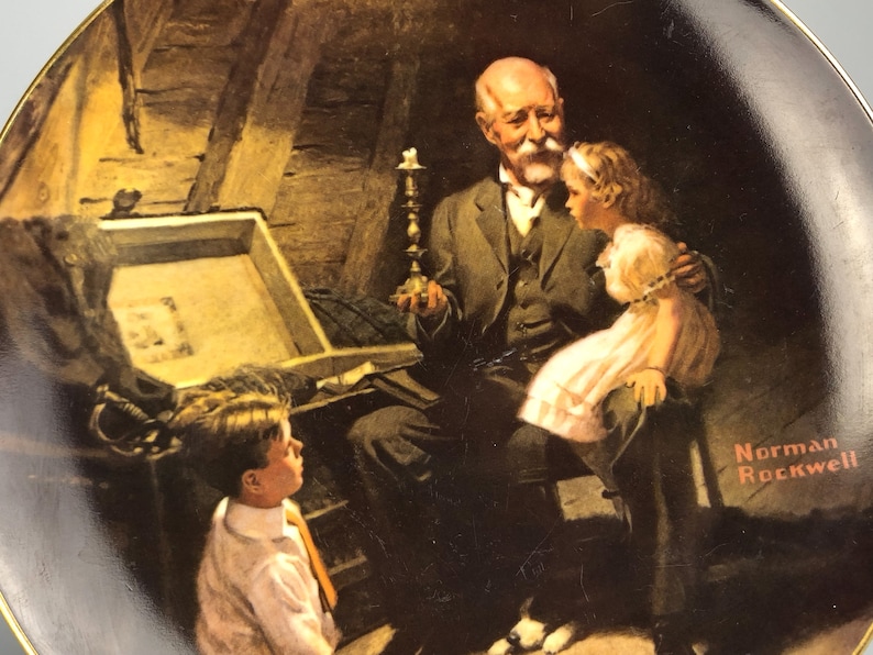 May include: A vintage-style porcelain plate featuring a painting by Norman Rockwell. The painting depicts an older man with a white beard, holding a candlestick, and two children looking at a treasure chest. The plate has a black background with a gold rim.
