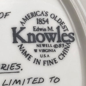 May include: A white ceramic plate with a black and white logo that reads "America's Oldest 1854 Edwin M. Knowles Name in Fine China Newell 83 W. Virginia U.S.A.". The plate also has the text "Series.  Ly Limited To" in black.