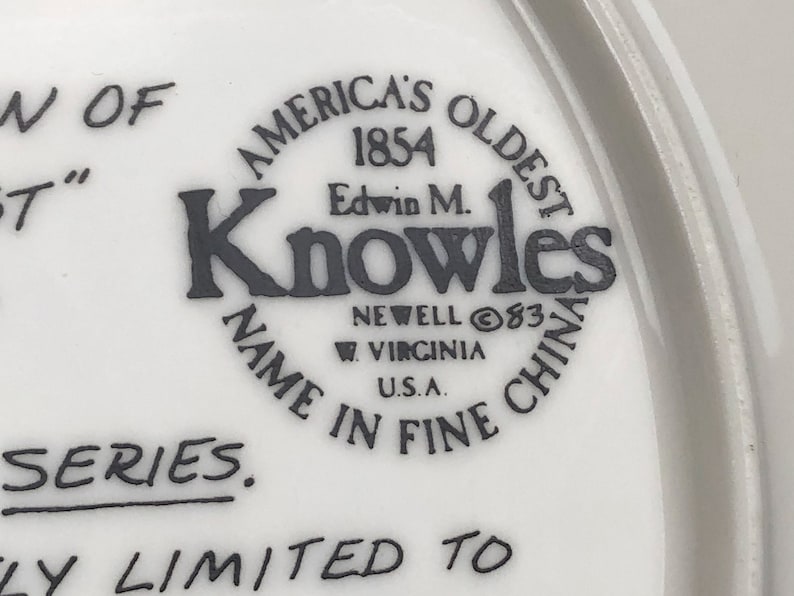 May include: A white ceramic plate with a black and white logo that reads "America's Oldest 1854 Edwin M. Knowles Name in Fine China Newell 83 W. Virginia U.S.A.". The plate also has the text "Series.  Ly Limited To" in black.