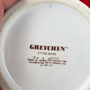 Pode incluir: Close-up da parte inferior de uma caneca de cer&acirc;mica branca com texto castanho que diz "GRETCHEN&trade; STONEWARE &copy; A.G. MCMLXXVII MADE IN JAPAN EXCLUSIVELY FOR CELEBRATION ARTS GROUP LTD IN THE UK"