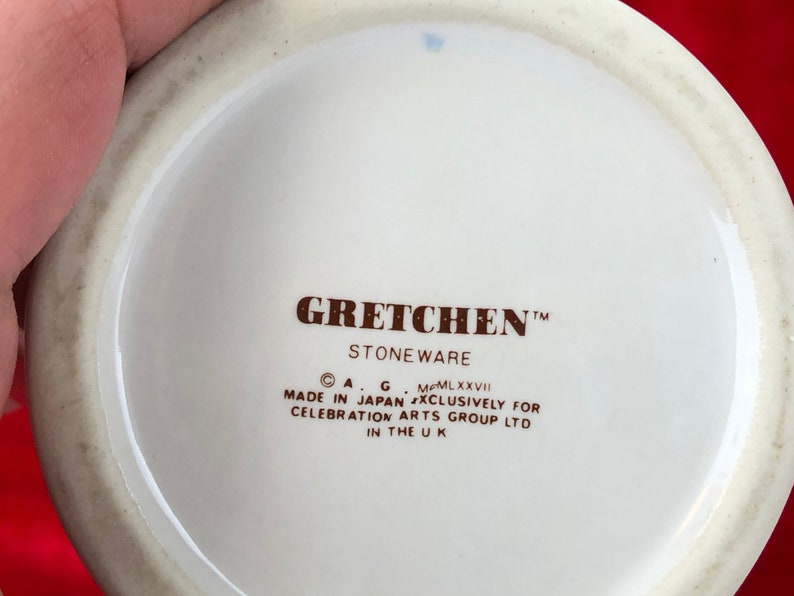 Pode incluir: Close-up da parte inferior de uma caneca de cer&acirc;mica branca com texto castanho que diz "GRETCHEN&trade; STONEWARE &copy; A.G. MCMLXXVII MADE IN JAPAN EXCLUSIVELY FOR CELEBRATION ARTS GROUP LTD IN THE UK"