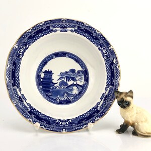 May include: A blue and white porcelain bowl with a gold rim and a traditional Chinese design. The bowl is decorated with a blue and white landscape scene with a pagoda, bridge, and trees.