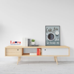 May include: A wooden media console with two drawers and a shelf. The console is light brown and has a white door on the right side. There are books and a plant on the shelf. A framed print with the text "Cafe Leche con When two become one" is hanging on the wall above the console.