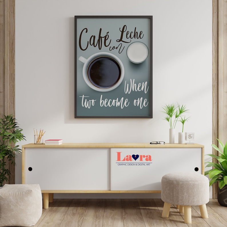 May include: A framed print with a blue background and white text that reads "Cafe Leche con When two become one". The print features a cup of coffee and a small pitcher of milk. The print is hanging on a white wall above a wooden cabinet.