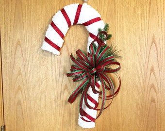 May include: A white and red candy cane Christmas wreath with a green and red bow. The wreath is hanging on a wooden door.